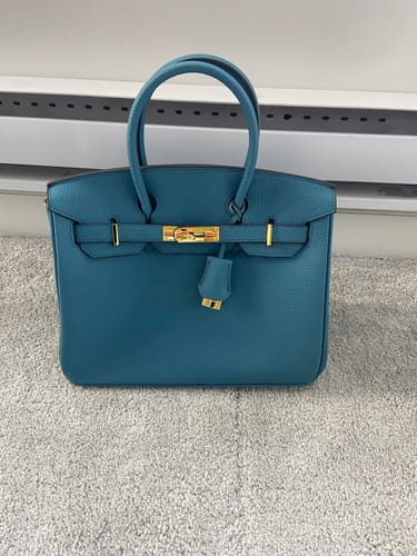 Reviewer's teal LALUVA Warkin Leather Bag with gold hardware, sitting on a grey carpet.