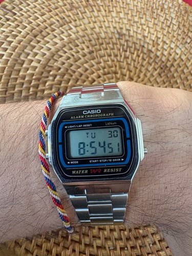 Primer plano del Reloj Casio Vintage A164WA-1VES plateado en la muñeca de un cliente, sobre un fondo tejido.