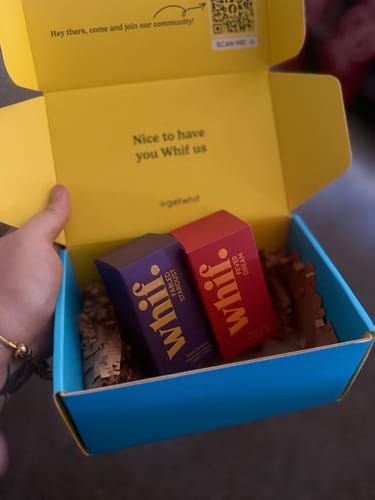 Customer holding open a branded delivery box with two colorful Whif perfume cartons inside.