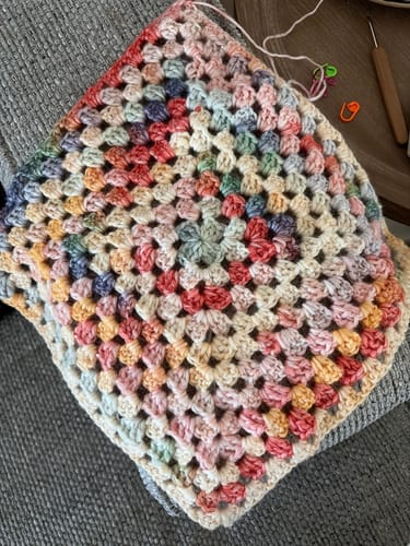 Customer's in-progress Hearthside Rainbow Blanket, crocheted into a colorful granny square on a sofa.