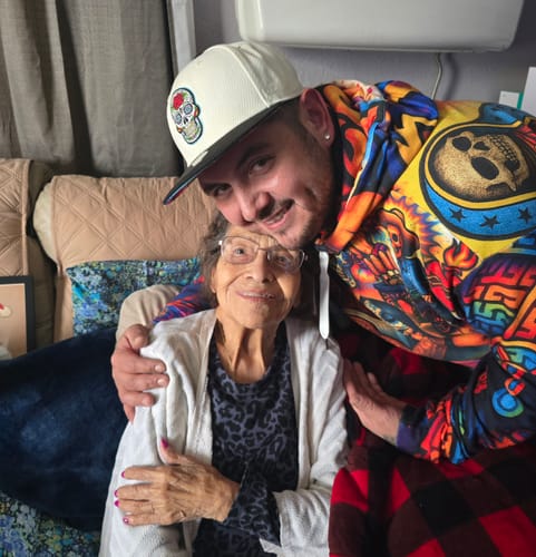 Customer smiling while wearing the colorful Raza Cultura All Over Print Hoodie and hugging an older woman.