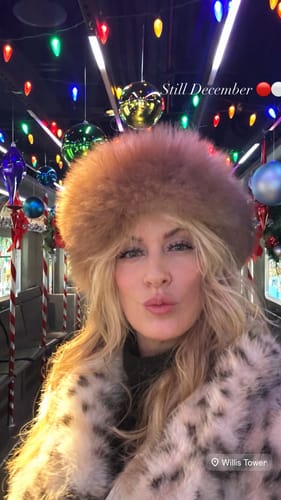 Reviewer in a fluffy hat and animal print coat, showing off their full Tulip Gossamer® Lashes on a festive bus.