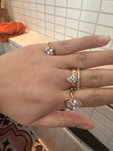 A reviewer's hand showing three gold Eterna Rings with pear-shaped stones being worn.