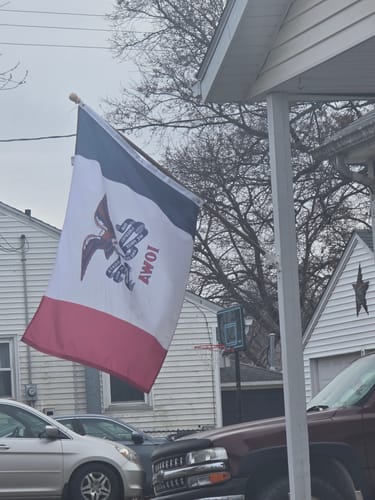 Customer's custom Iowa-style flag with a military emblem flying from a pole outside a house.