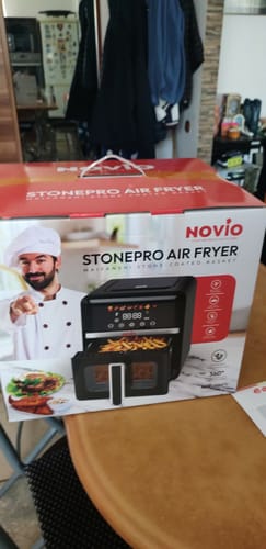 Imagine de la un client cu cutia produsului Air Fryer Novio StonePro pe o masă de lemn.