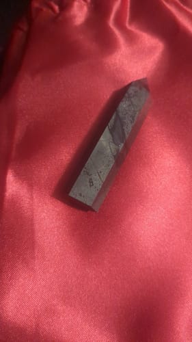 Customer's marbled hematite crystal point from the VIP Crystal Club resting on a red satin pouch.