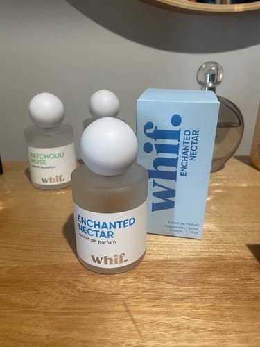 Customer's bottle of Enchanted Nectar perfume on a wooden surface with its light blue box and other perfumes in the background.