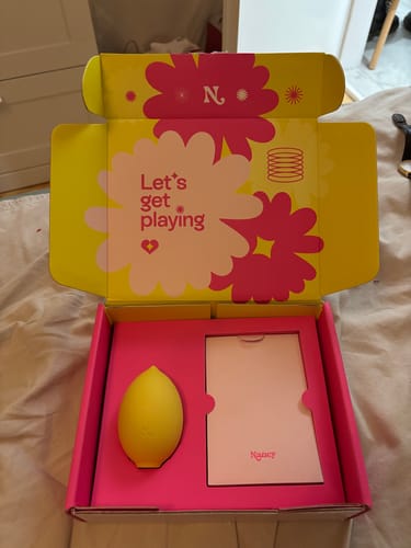 Reviewer unboxing the Lem Clitoral Massager, showing the yellow device inside its vibrant packaging.