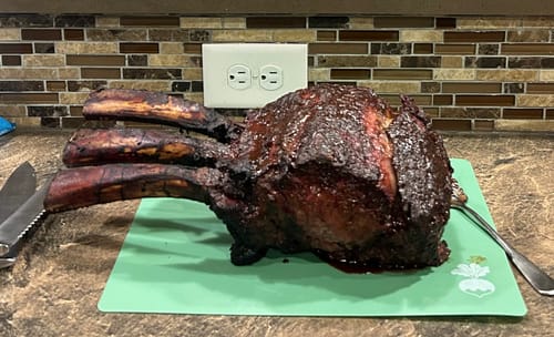 Customer's cooked Tomahawk Prime Rib Roast with three large bones resting on a green cutting board.