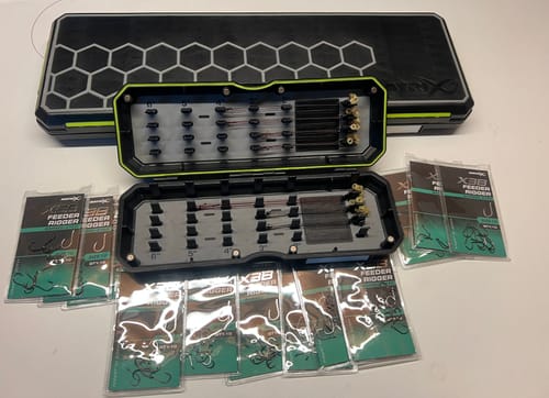 Beoordelaar toont X3B Feeder Rigger haken in de verpakking en geordend in een zwarte rigbox.