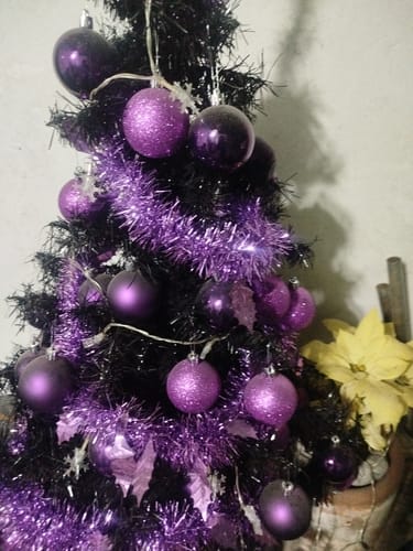Un cliente muestra el set de esferas de Navidad fucsia decorando un árbol negro.