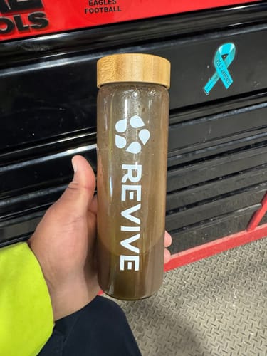 Customer holding a Revive brand bottle filled with the dark Mushroom Complex drink in a workshop setting.