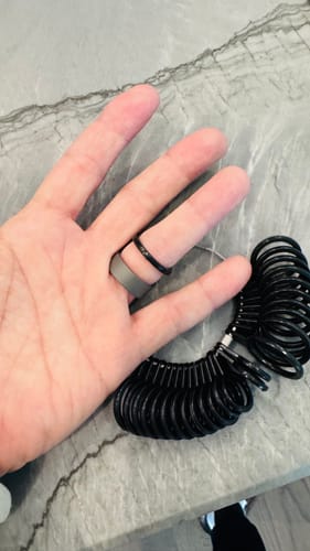 Customer's hand holding the Thorum Ring Sizer set while trying a black sizer ring on a finger next to a grey ring.