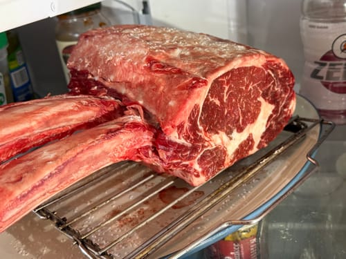 Customer's large, raw Tomahawk Prime Rib Roast resting on a wire rack inside a refrigerator.