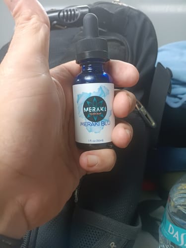 Customer's hand holding the small, blue bottle of Meraki Blu.