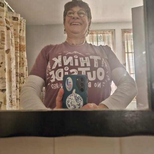 Reviewer smiling in a mirror selfie, wearing the maroon Think Outside T-shirt layered over a long-sleeved shirt.