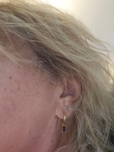Customer's close-up of the Bella Birthstone Huggies Earring, a gold hoop with a dangling dark rectangular stone, worn in-ear.