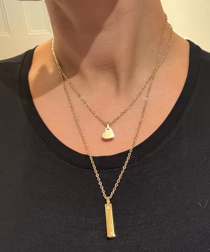Reviewer wearing the gold Minimalist Heart Urn Pendant layered with a second necklace against a black shirt.