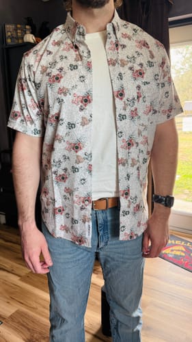 Customer wears the Stranger Things KUNUFLEX shirt open over a white tee, showing the fit and floral pattern.