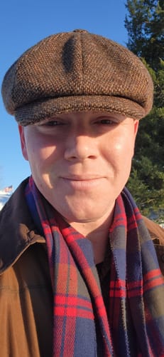 Reviewer in a close-up photo wearing the brown tweed JP Cap outdoors.