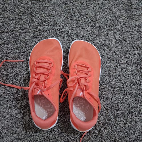 Arvostelijan oranssit Vaistoa Tahto -paljasjalkasalikengät harmaalla matolla ylhäältä kuvattuna.