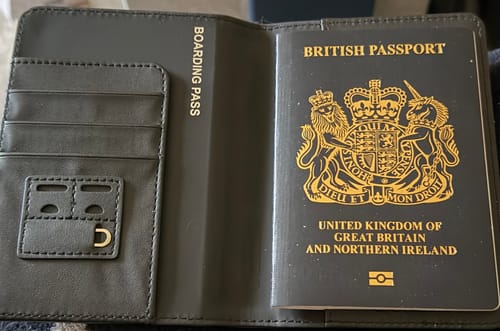 Customer's dark grey Trackable Passport Cover shown open, holding a British passport and revealing document slots.