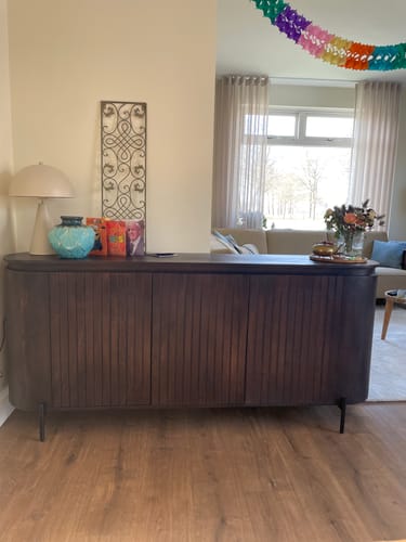 Recensent toont het donkerbruine by fonQ Grand Dressoir dat in een woonkamer tegen een muur staat.