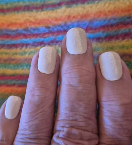 Nahaufnahme der Nägel einer Kundin, die das 'In The Buff!' UV-Gel mit einem goldenen Glitzer-Überlack aufgetragen hat.