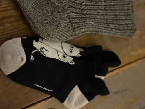 Närbild på ett par svarta Mumin ankelstrumpor med vita motiv som ligger på ett träbord.