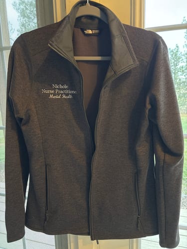 Customer's embroidered dark grey North Face Skyline Full-Zip jacket hanging on a hanger.