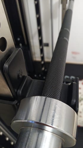 Reviewer's close-up of the Garage Strength Bar's coarse knurling and chrome sleeve resting in a rack.