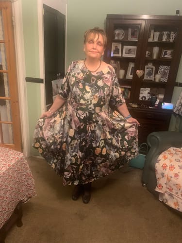 Reviewer standing in a living room, holding out the wide skirt of a dress made from the Ink Wash Bloom Stretch Velvet Fabric.