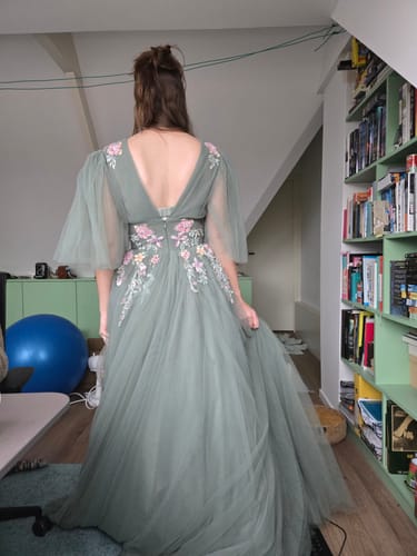 Reviewer shows the back of the sage green Sage Verse Gown with its V-back, floral embroidery, and custom sheer sleeves.