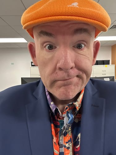 Reviewer wearing the Cal Ripken Jr. 'The Iron Man' shirt under a blue blazer and orange hat in a close-up selfie.