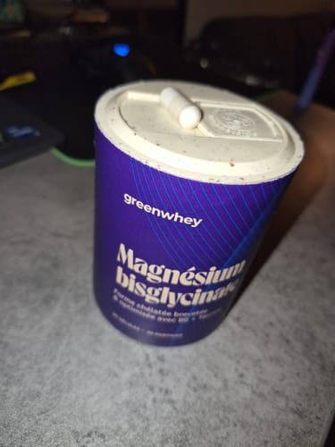 Un client montre le pot violet de Magnésium Bisglycinate avec une gélule blanche posée sur le couvercle.