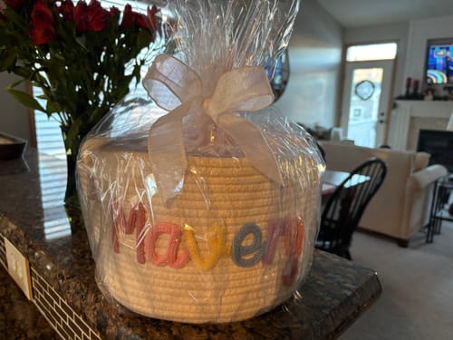Customer's personalized knitted basket with the name 'Mavery' in multicolor yarn, wrapped in cellophane with a bow.