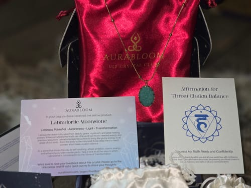 Customer's AuraBloom Subscription Box contents, including a green pendant necklace, a red pouch, and two informational cards.
