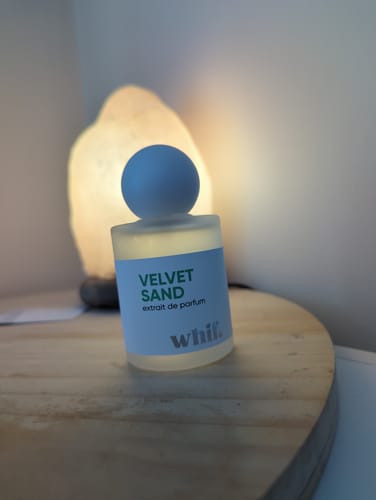 Customer's bottle of Velvet Sand perfume sits on a wooden surface, backlit by a warm lamp.