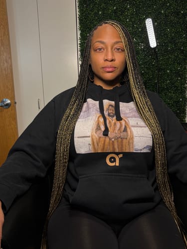 Reviewer sitting in a chair wearing black leggings and a hoodie, showing their braided hair.