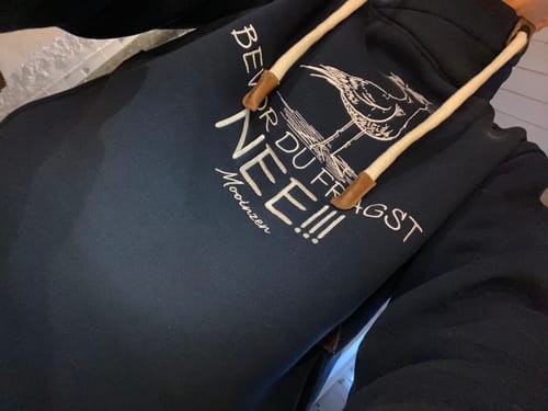 Ein Kunde trägt einen dunkelblauen Hoodie mit einem großen weißen Stickmotiv einer Möwe und einem Spruch.
