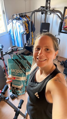 Clienta sonriente mostrando su paquete de Gomitas Creatina en un gimnasio casero.