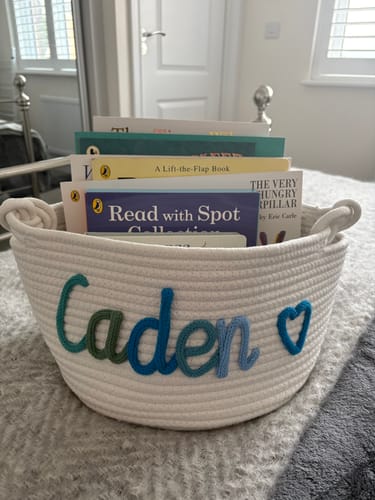 Customer's personalized woven basket with the name 'Caden' embroidered on it, shown holding children's books.