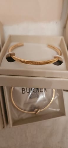 Close-up of a reviewer's gold-colored Violet Bracelet resting in its white presentation box.