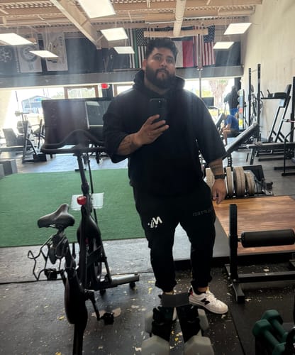 Customer taking a mirror selfie in a gym, wearing the black Megàlo 3/5 Sleeve Hoodie.