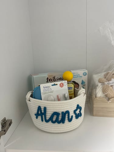 Reviewer's personalized knitted basket in white, featuring the name 'Alan' and a star in blue yarn, filled with baby items.