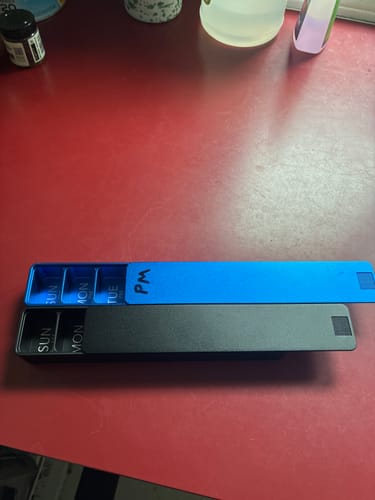 Customer's blue and black Weekly AM-PM Vitamin Case 2.0 shown separated on a red table to display their size.