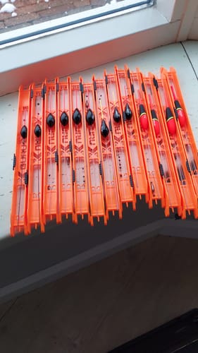 Recensent toont een rij oranje RIG WINDERs met diverse dobbers en vislijnen erop gewonden.