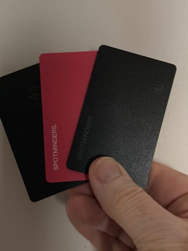 Customer holding three fanned-out SPOTMINDERS Tracking Cards, two black and one red.