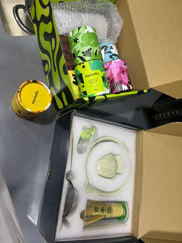 Cliente desempaquetando un kit de preparación y varias latas coloridas de Té Matcha Premium.