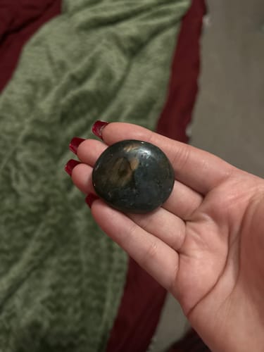 Reviewer holding a dark, polished labradorite moonstone crystal in their palm.